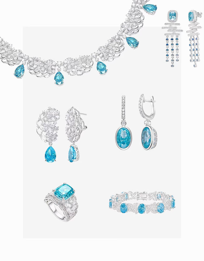 The Gem Vivi Cadence Cascade Earrings, crafted in silver and adorned with aquamarine cubic zirconia, are featured among a collection of blue gemstone jewelry displayed on a white background.