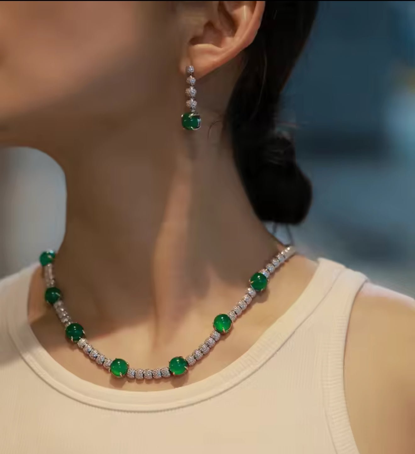 A woman wearing a sleeveless beige top, an emerald and diamond necklace with pavé diamond beads, and Gem Vivi Chalcedony Cabochon Drop Earrings.