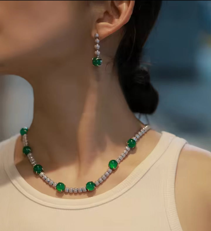 A woman wearing a sleeveless beige top, an emerald and diamond necklace with pavé diamond beads, and Gem Vivi Chalcedony Cabochon Drop Earrings.