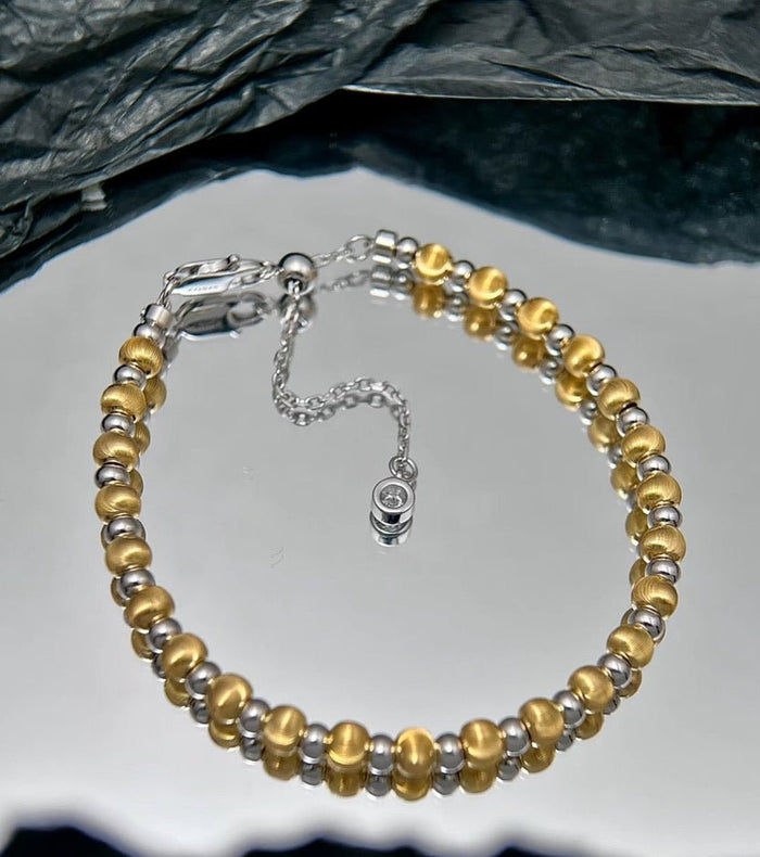 The Gem Vivi Glow Dual Tone Bead Bracelet, crafted with 18K Yellow Gold and 925 Sterling Silver beads plus extender and clasp, is elegantly displayed on a reflective surface.