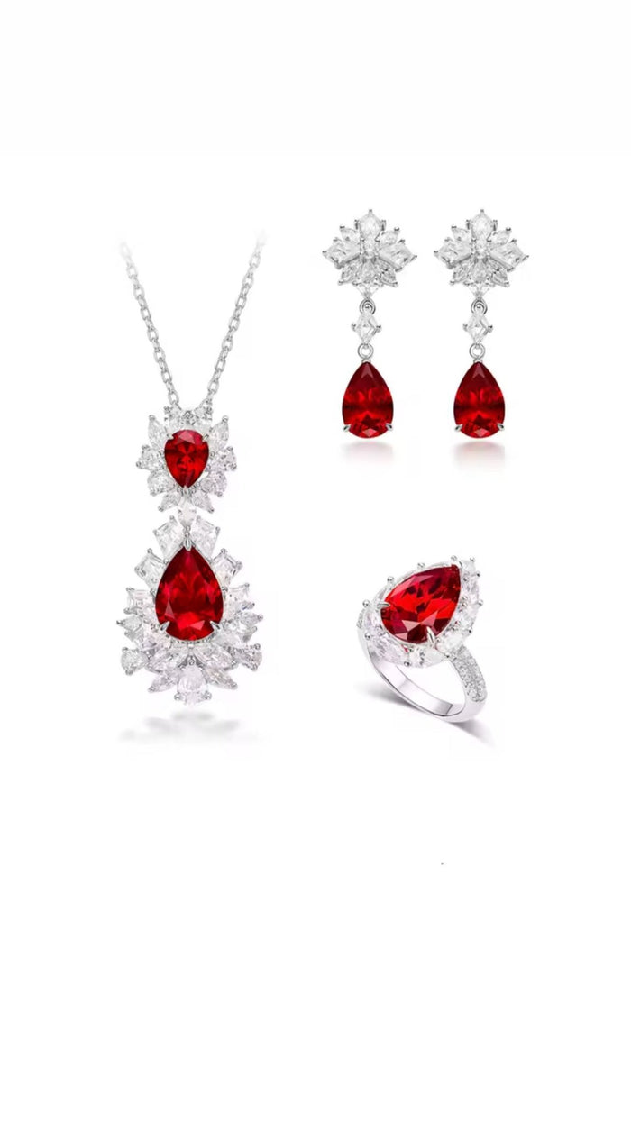 A jewelry set featuring a necklace, ring with pear-cut rubies and clear stones, and Gem Vivi’s Caroline Ruby Teardrop Starburst Earrings in 18k white gold, all displayed on a white background.