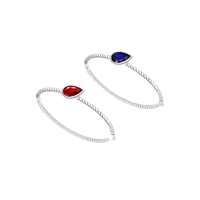 Gem Vivi’s Blue Sapphire and Ruby Teardrop Bracelet features sterling silver bangles, each with a teardrop-shaped gemstone—vibrant ruby and striking blue sapphire—in a minimalist design.