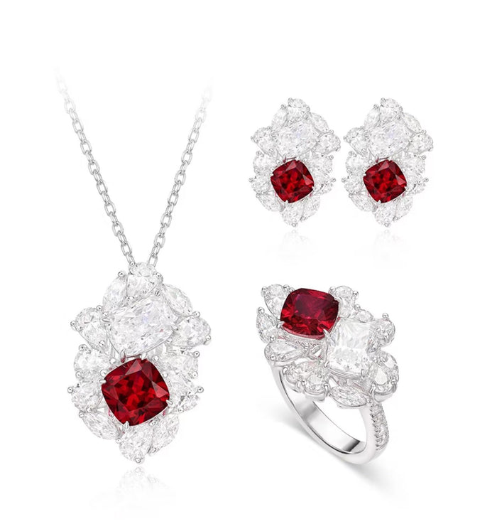 The Gem Vivi Calista Bloom Ruby Ring jewelry set includes a necklace, earrings, and a lab-created ruby ring, each featuring a central red gemstone encircled by clear stones in elegant silver settings.
