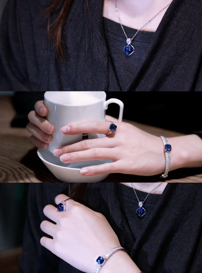Wearing a Gem Vivi Blue cabochon Bracelet with a matching necklace and ring in sterling silver, a person dressed in dark attire holds a white mug and saucer.