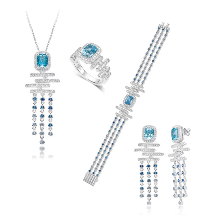 The Gem Vivi Cadence Cascade Necklace is shown with a matching ring, bracelet, and earrings featuring blue gemstones and silver accents, all beautifully arranged on a white background.