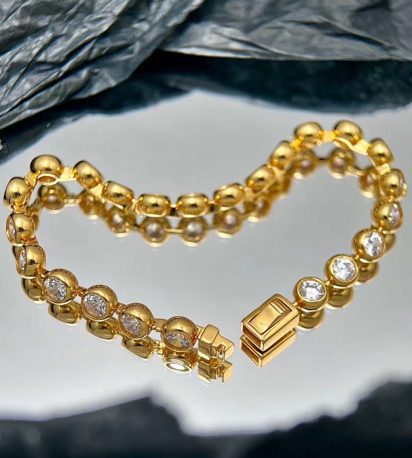 The Radiance Bezel Bracelet by Gem Vivi is crafted in 18K yellow gold, featuring round cubic zirconia stones set in a heart shape on a reflective, textured surface.