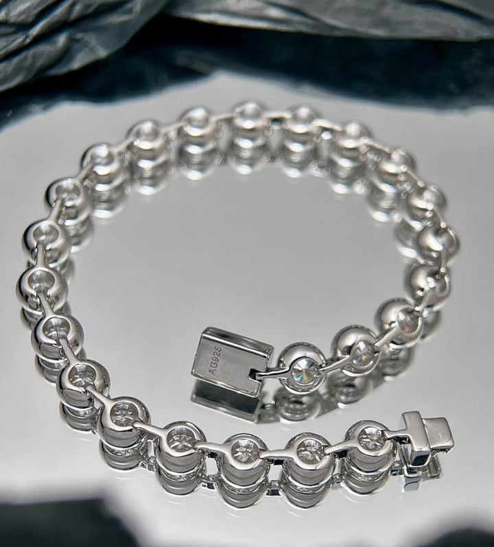 The Gem Vivi Radiance Bezel Bracelet features round, bezel-set cubic zirconia stones and a box clasp, shown on a reflective surface.