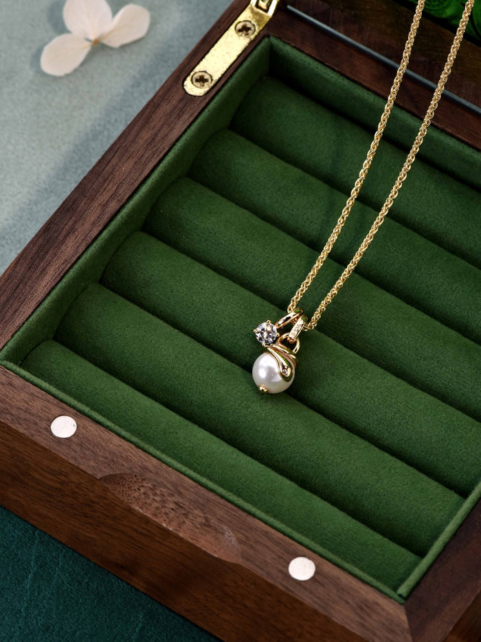 The Gem Vivi Serpentine Charm Necklace features a shell pearl and gemstone pendant on 18K yellow gold, elegantly presented in a green velvet-lined wooden box.
