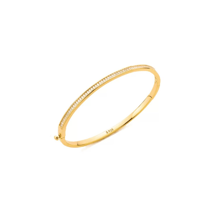 The Gem Vivi Hinged Baguette Glow Bangle Bracelet features 18K yellow gold and a row of clear cubic zirconia stones set along the top edge, shown against a white background.