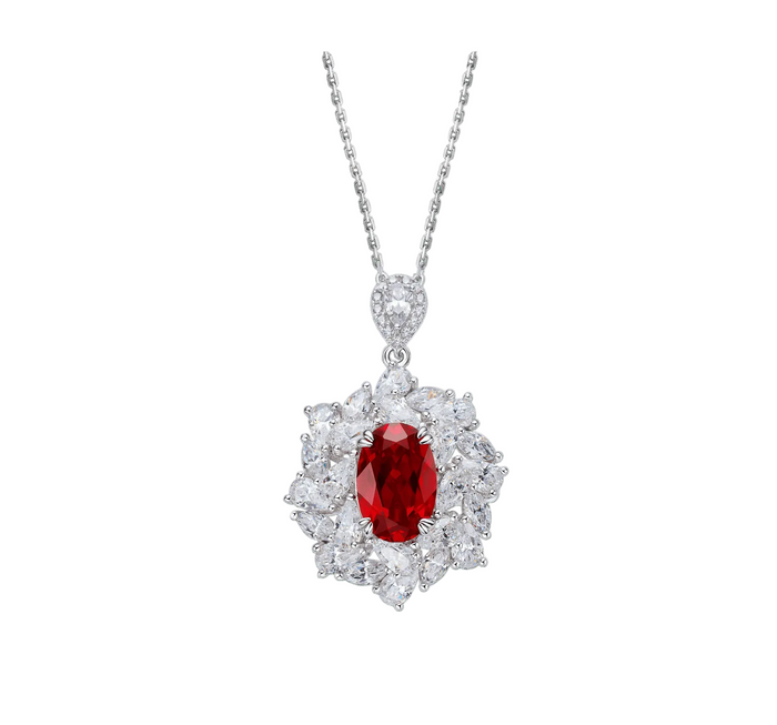 The Blossom Ruby Pendant Necklace by Gem Vivi features an oval red lab-created ruby framed by a halo of clear faceted stones, set on a fine silver chain.