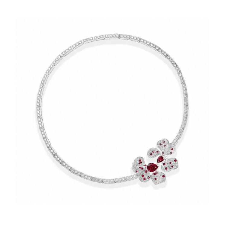The Crimson Petal Blossom Tennis Necklace by Gem Vivi features a geometric floral pendant with emerald-cut ruby gemstones in a symmetrical 18k white gold design.