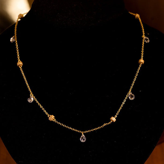 The Raindrop Gold Necklace by Gem Vivi features small round 18K gold beads and clear teardrop cubic zirconia pendants, elegantly displayed on a black velvet bust.