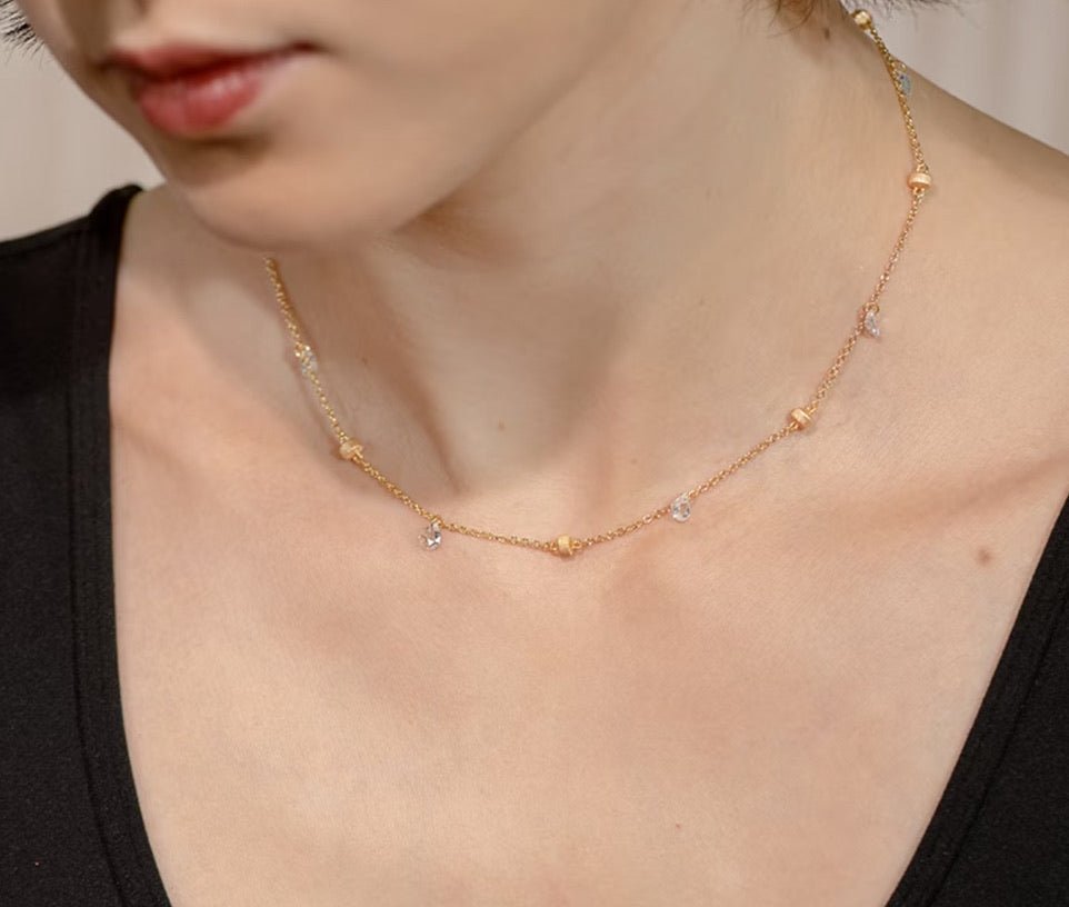 A person wearing the Raindrop Gold Necklace by Gem Vivi, featuring 18K gold with small bead and crystal accents, paired with a black V-neck top.