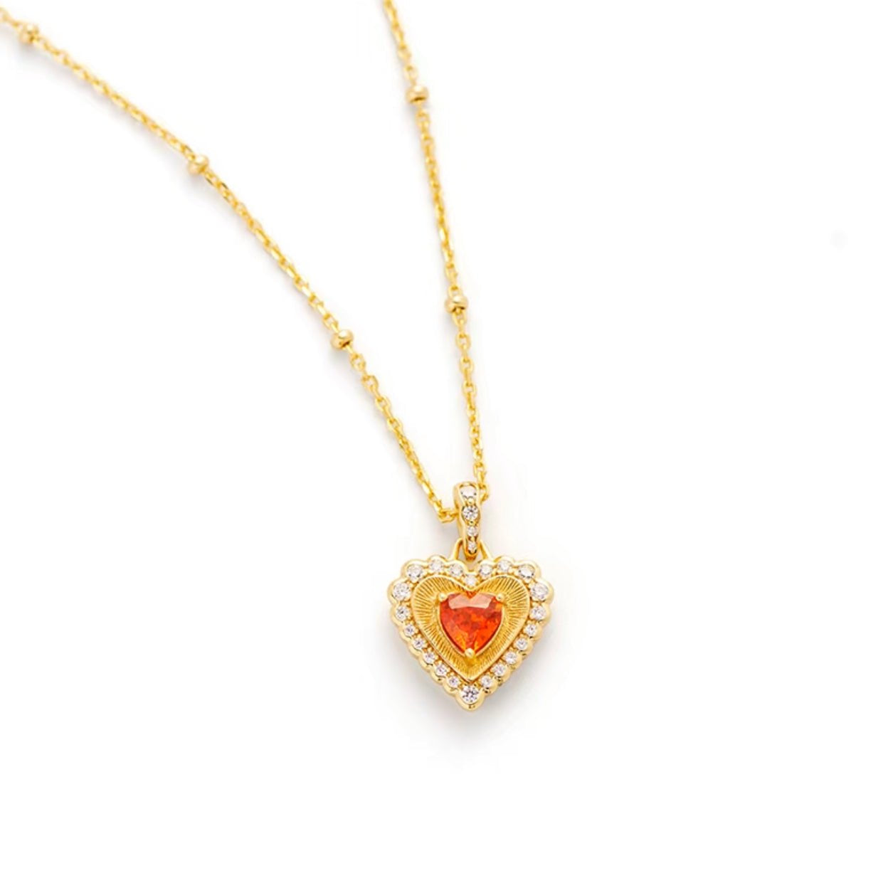 The Gem Vivi Heart Ember Halo Necklace features a heart-shaped pendant with an orange gemstone center, haloed by sparkling cubic zirconia on a delicate 18K yellow gold chain.