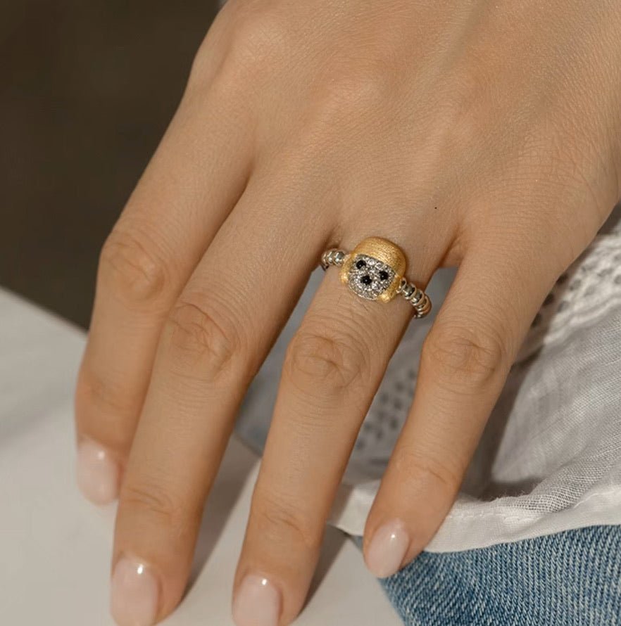 A close-up of a hand wearing Gem Vivi’s Dog In Golden Hat Ring on the middle finger, crafted in 18K yellow gold with a unique design. The nails are neatly manicured with nude polish.
