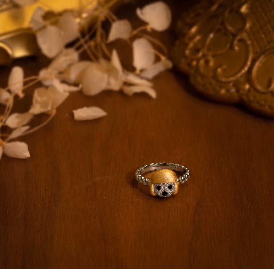 A Gem Vivi Dog In Golden Hat Ring rests on a wooden surface, with dried leaves and decorative golden objects in the background.