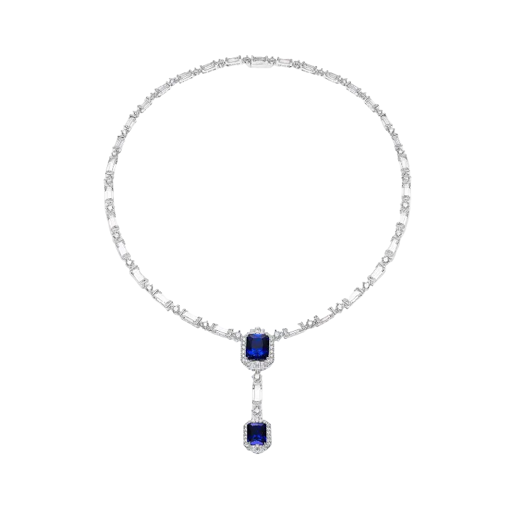The Blue Midnight Cascade Necklace by Gem Vivi showcases two emerald-cut sapphires in 18k white gold, each haloed by sparkling diamonds, elegantly arranged in a cascading drop design.