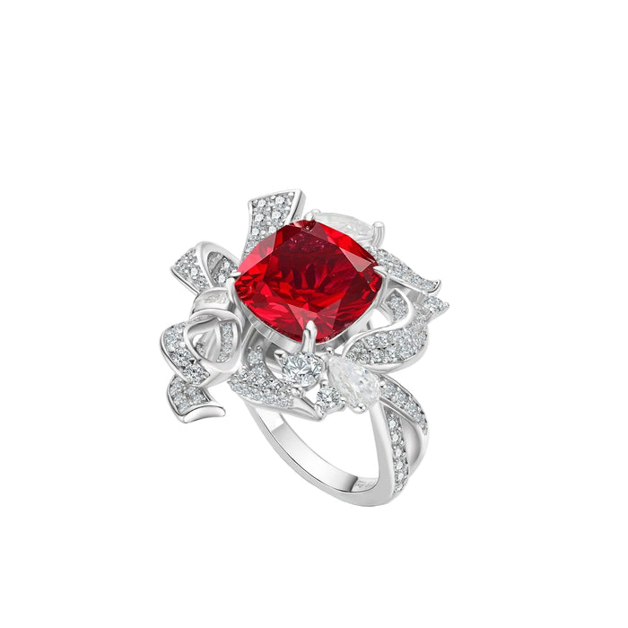 The Gem Vivi Bloom Ribbon Ring showcases a large cushion-cut ruby at its center, accented by ribbon-inspired details and shimmering clear gemstones.