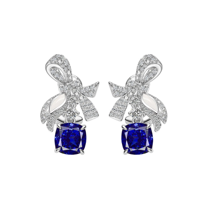 The Gem Vivi Blue Sapphire Drop Ribbon Earrings feature 18k white gold bow-shaped tops with clear stones and dangling square-cut deep blue sapphires.