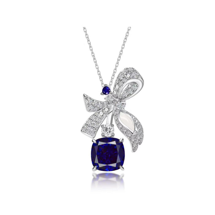 The Gem Vivi Blue Sapphire Drop Ribbon Pendant Necklace showcases a diamond-studded bow ribbon and a large cushion-cut sapphire, all elegantly crafted in 18k white gold.