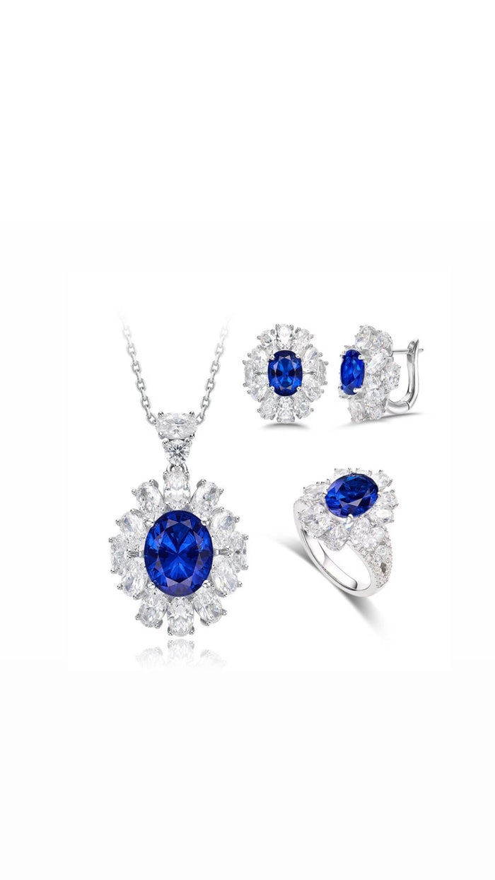 The Bloom Royal Halo Ring by Gem Vivi is part of a jewelry set with a lab-created sapphire necklace, matching stud earrings, and an heirloom-inspired ring—all accented with clear stones in silver settings.