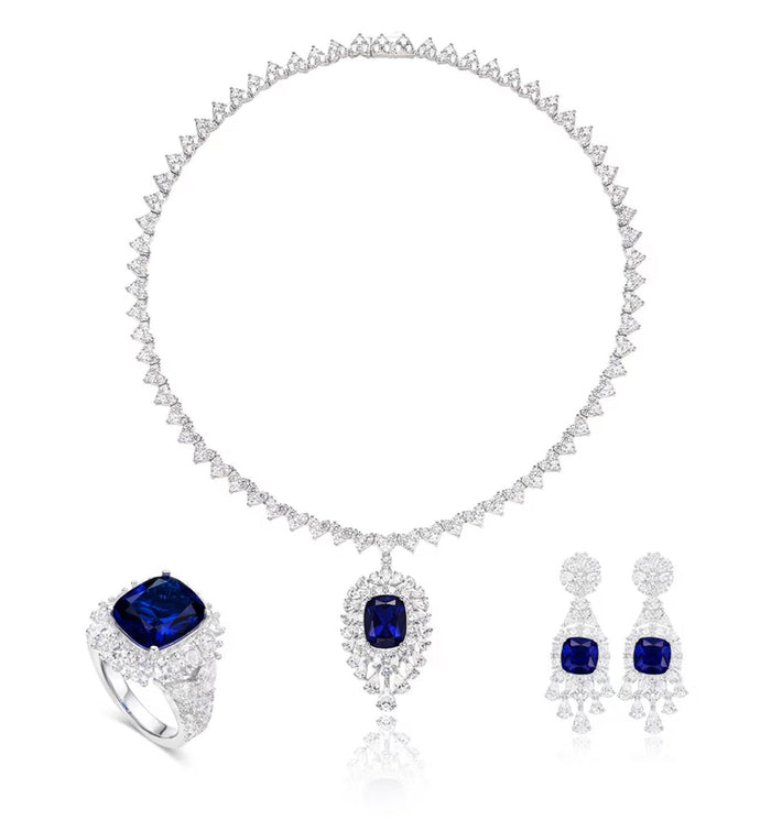 A jewelry set featuring a diamond necklace and pendant, matching earrings, and the Gem Vivi Blue Sapphire Royal Eclipse Ring in 18k white gold, each accented with a deep blue lab-created sapphire.