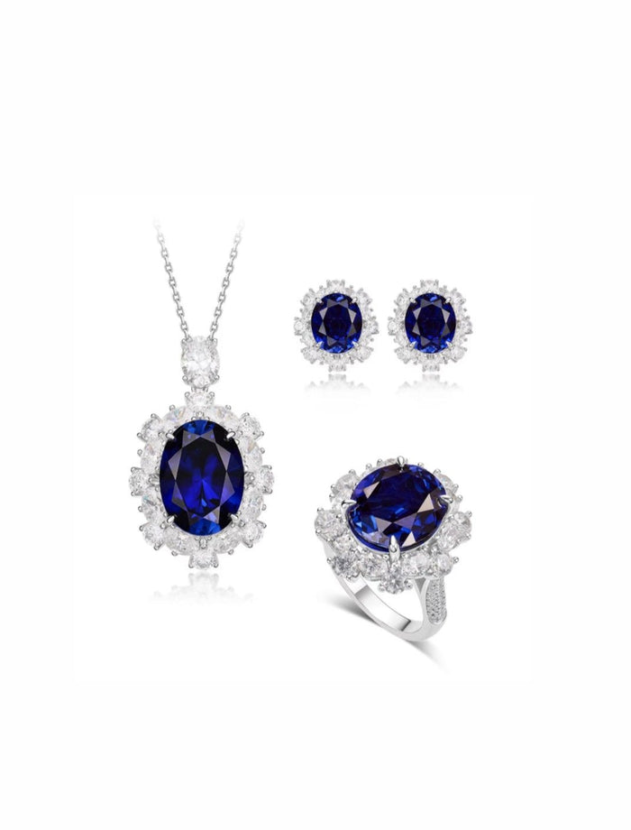 The Gem Vivi Blue Sapphire Large Halo Pendant Necklace features an oval lab-created sapphire surrounded by small clear stones, set in 18k white gold plated silver. Matching earrings and ring available.