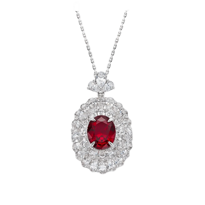 The Clara Ruby Radiance Pendant Necklace by Gem Vivi features a large oval lab-created ruby, accented with two rows of clear diamonds in an ornate silver setting.