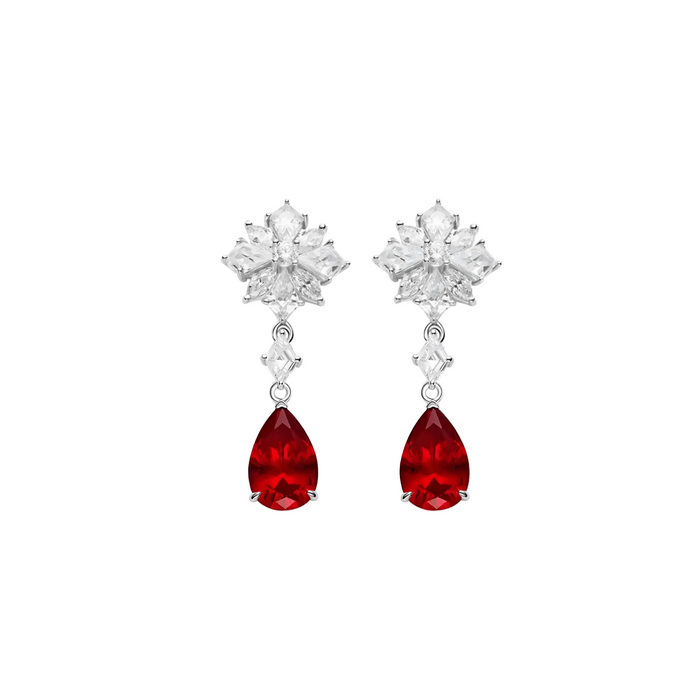The Caroline Ruby Teardrop Starburst Earrings by Gem Vivi feature snowflake-shaped tops with pear-cut rubies suspended below, all elegantly set in 18k white gold.