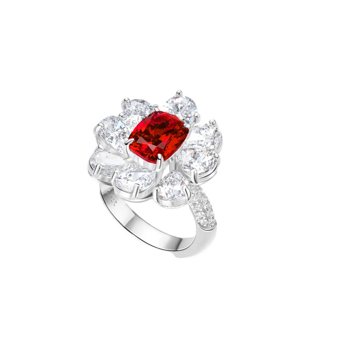 The Carissa Ruby Petal Ring by Gem Vivi showcases a central rectangular lab-created ruby, encircled by pear-shaped clear stones in a floral design and accented with small stones along the band.