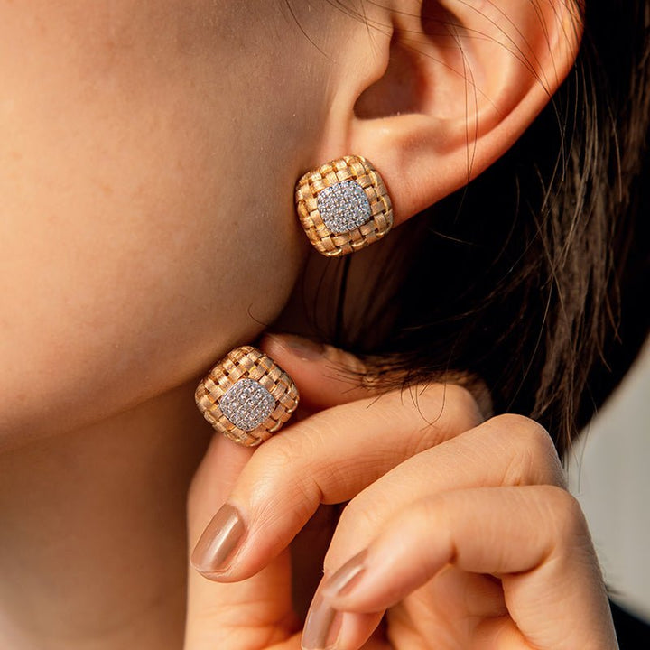 A person wearing Gem Vivi’s Woven Luxe Cushion Studs, featuring a square gold and silver woven design, accented with a sparkling cluster of Cubic Zirconia crystals at the center.